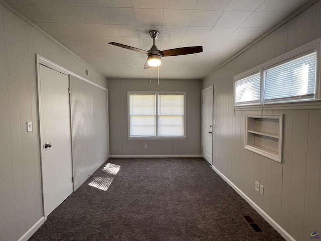 unfurnished bedroom featuring carpet, multiple windows, a closet, crown molding, and wooden walls