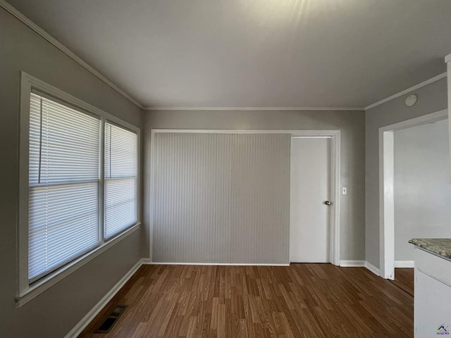 unfurnished dining area featuring dark wood-type flooring, crown molding, and baseboards
