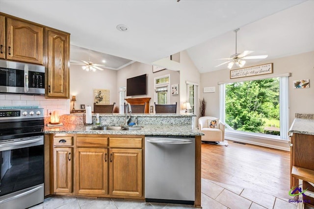 kitchen with stainless steel appliances, ceiling fan, a sink, open floor plan, and vaulted ceiling