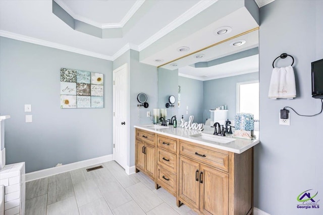 bathroom with a raised ceiling, double vanity, ornamental molding, baseboards, and recessed lighting