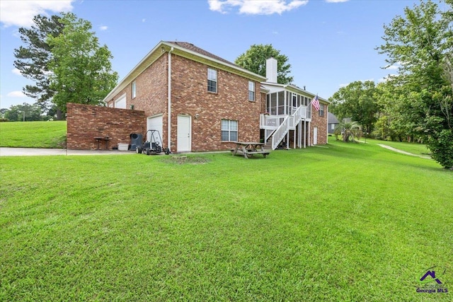 rear view of house featuring a sunroom, a chimney, brick siding, and a lawn