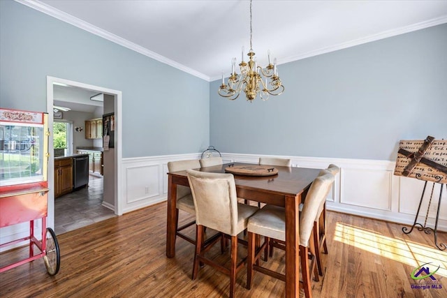 dining room featuring a chandelier, ornamental molding, wood finished floors, wainscoting, and a decorative wall