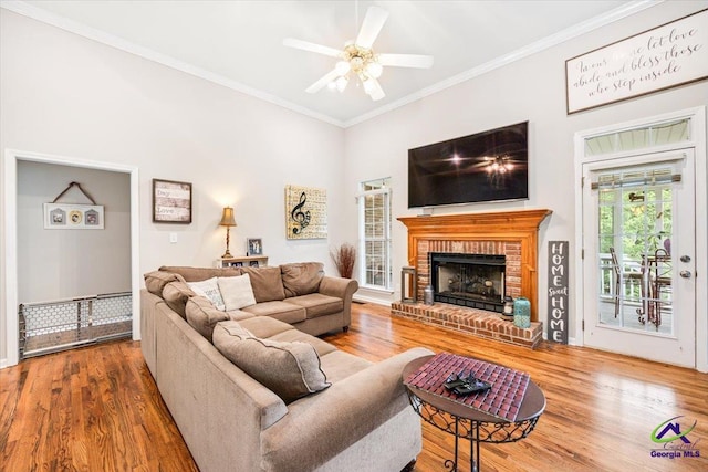 living room featuring ornamental molding, wood finished floors, a brick fireplace, a ceiling fan, and baseboards