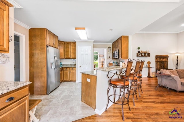 kitchen with appliances with stainless steel finishes, a peninsula, a breakfast bar area, brown cabinets, and backsplash