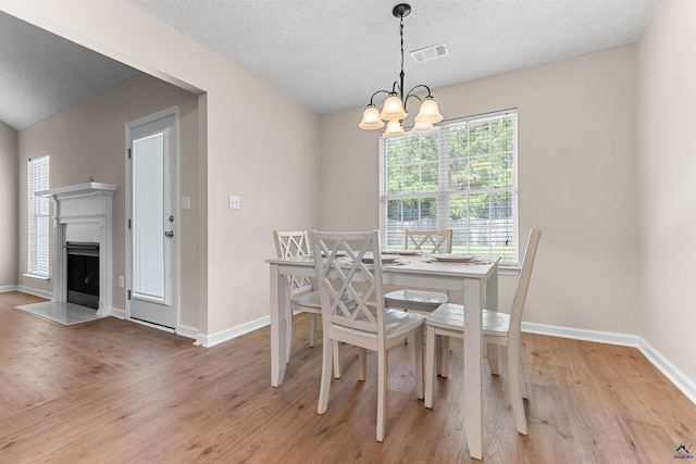 dining area featuring light wood-style floors, a chandelier, baseboards, a textured ceiling, and a fireplace with flush hearth