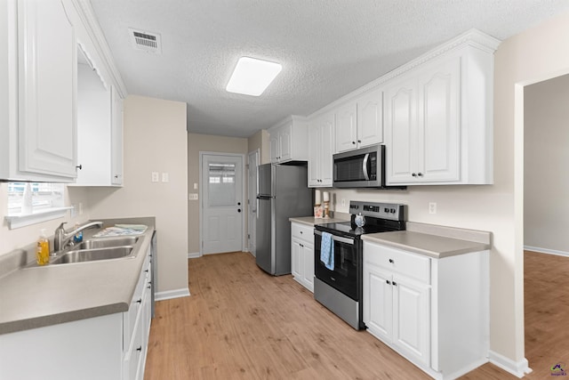 kitchen featuring stainless steel appliances, a sink, light wood-style floors, white cabinetry, and a textured ceiling