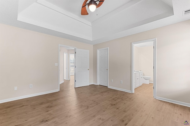 unfurnished bedroom with a raised ceiling, light wood-style flooring, baseboards, and ensuite bath