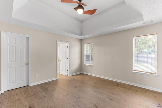 unfurnished bedroom featuring a raised ceiling, wood finished floors, baseboards, ensuite bath, and ceiling fan
