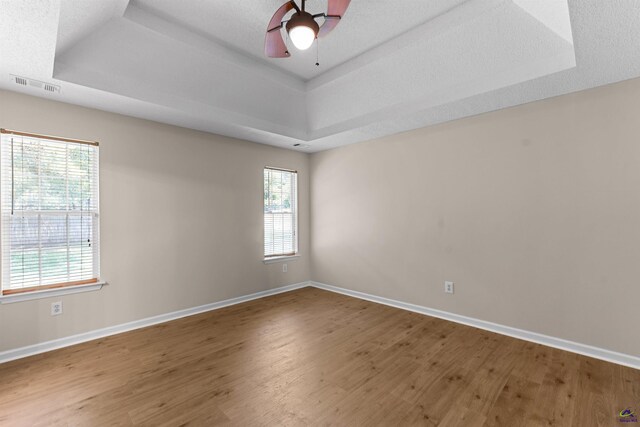 unfurnished room featuring a tray ceiling, wood finished floors, baseboards, and ceiling fan