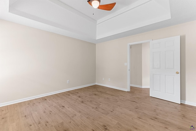 empty room featuring a raised ceiling, a ceiling fan, and light wood-type flooring