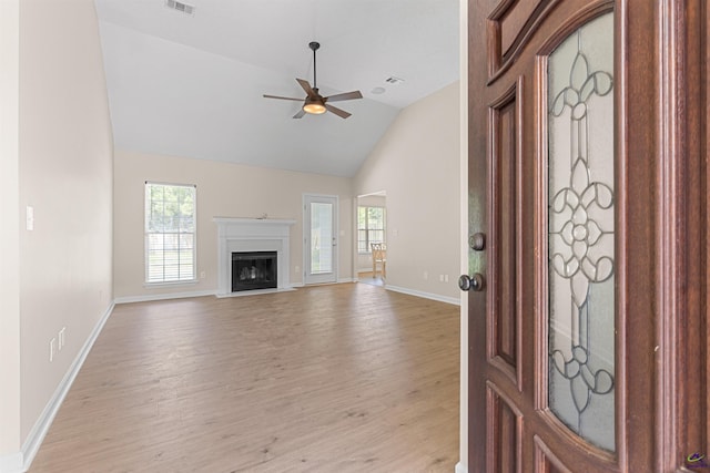 unfurnished living room featuring light wood-type flooring, high vaulted ceiling, baseboards, a ceiling fan, and a fireplace with raised hearth