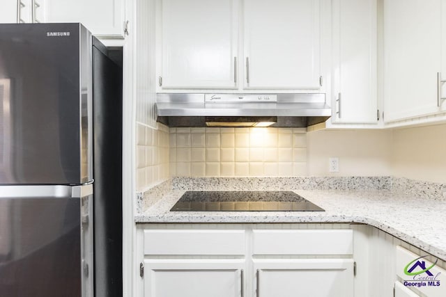 1035 S Pine Knoll Dr, Macon, GA 31204 - kitchen with freestanding refrigerator, black electric stovetop, under cabinet range hood, white cabinetry, and backsplash