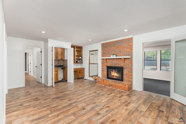 207 Oak Forest Ln, Warner Robins, GA 31088 - unfurnished living room featuring light wood-style flooring, recessed lighting, a brick fireplace, baseboards, and crown molding