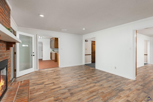 207 Oak Forest Ln, Warner Robins, GA 31088 - unfurnished living room featuring a brick fireplace, wood finished floors, crown molding, recessed lighting, and a textured ceiling