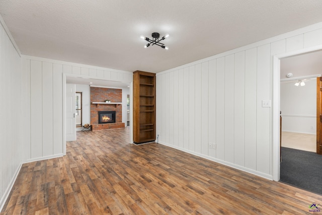 207 Oak Forest Ln, Warner Robins, GA 31088 - unfurnished living room featuring dark wood-style flooring, a fireplace, a textured ceiling, baseboards, and a decorative wall
