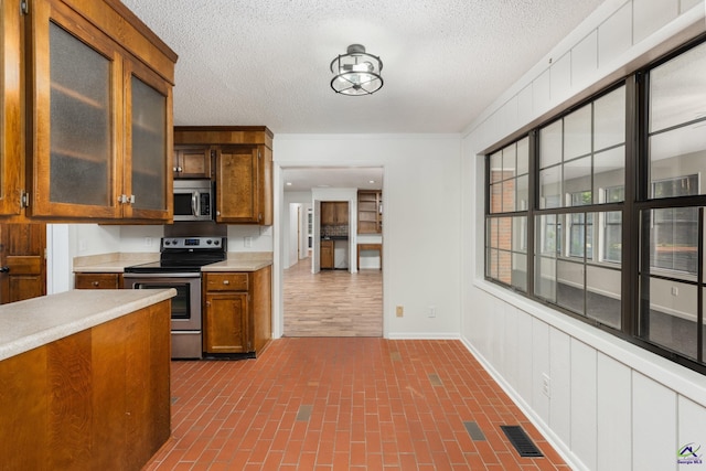 207 Oak Forest Ln, Warner Robins, GA 31088 - kitchen featuring stainless steel appliances, light countertops, brick patterned flooring, glass insert cabinets, and brown cabinets