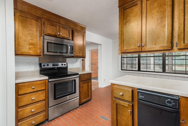 207 Oak Forest Ln, Warner Robins, GA 31088 - kitchen featuring appliances with stainless steel finishes, brick patterned floors, light countertops, brown cabinetry, and a textured ceiling