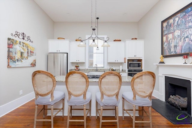1360 Calhoun St, Macon, GA 31201 - kitchen with appliances with stainless steel finishes, a kitchen breakfast bar, white cabinets, hanging light fixtures, and dark wood-style flooring