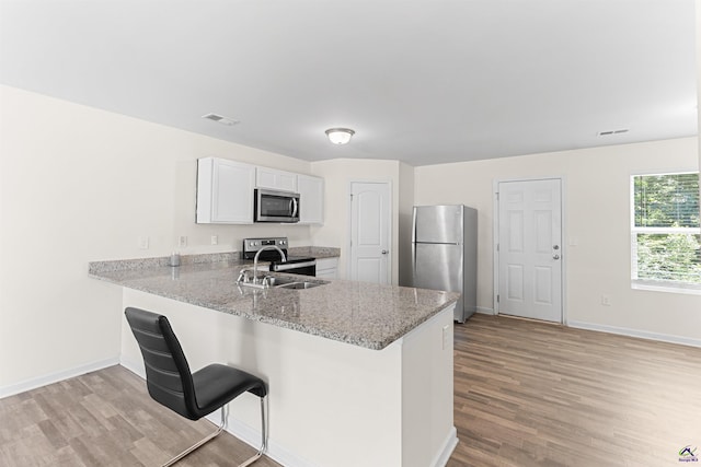 630 Ivy Brook Way, Macon, GA 31210 - kitchen with appliances with stainless steel finishes, light wood-style floors, a peninsula, light stone counters, and white cabinetry