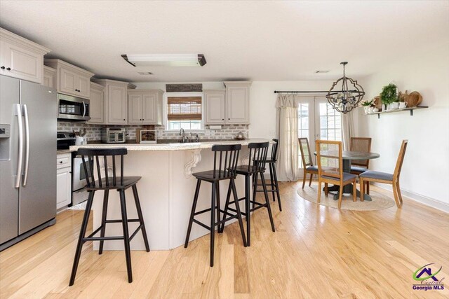 133 Gage Dr, Perry, GA 31069 - kitchen featuring appliances with stainless steel finishes, a chandelier, light wood finished floors, backsplash, and a breakfast bar area