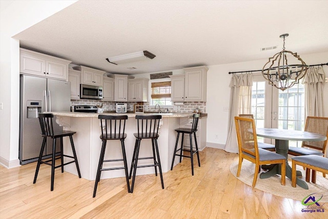 133 Gage Dr, Perry, GA 31069 - kitchen with stainless steel appliances, a chandelier, backsplash, light wood-type flooring, and a breakfast bar