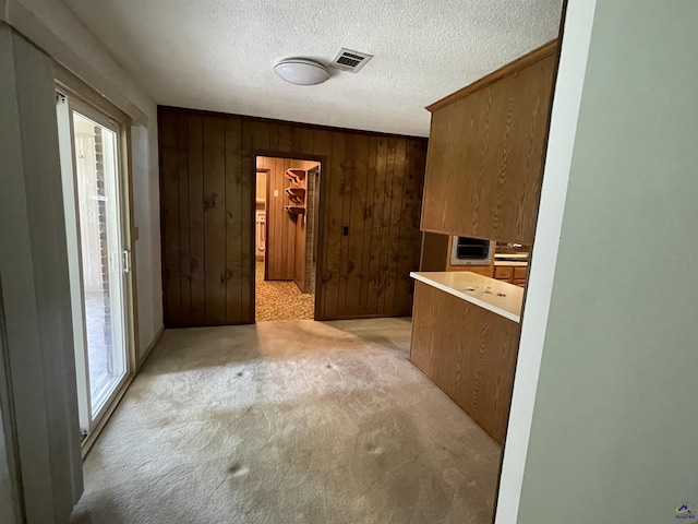122 Cheryl Blvd, Warner Robins, GA 31088 - kitchen featuring light colored carpet, wooden walls, a textured ceiling, brown cabinetry, and light countertops