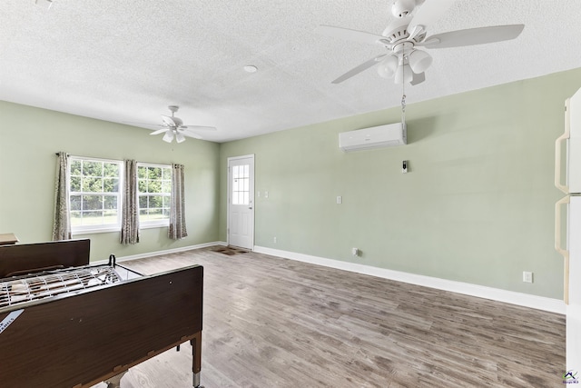 2725 Moseley Rd, Byron, GA 31008 - unfurnished bedroom with an AC wall unit, a textured ceiling, light wood finished floors, baseboards, and a ceiling fan
