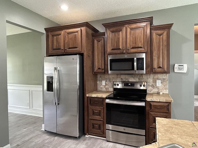 228 Piedmont Ln, Bonaire, GA 31005 - kitchen with appliances with stainless steel finishes, light countertops, light wood-style flooring, tasteful backsplash, and wainscoting