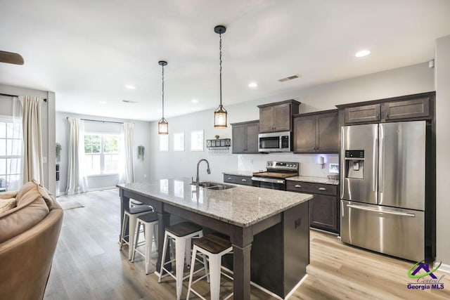 501 Adirondac Way, Bonaire, GA 31005 - kitchen with appliances with stainless steel finishes, dark brown cabinets, a kitchen breakfast bar, an island with sink, and light stone countertops