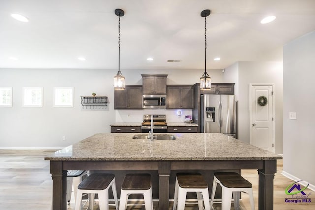 501 Adirondac Way, Bonaire, GA 31005 - kitchen featuring appliances with stainless steel finishes, a breakfast bar area, dark brown cabinetry, light wood finished floors, and a kitchen island with sink