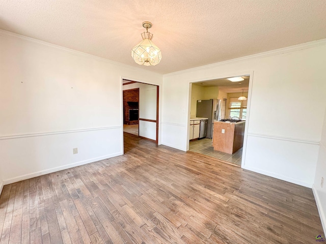 7285 Nowell Rd S, Macon, GA 31216 - unfurnished room with a textured ceiling, wood finished floors, crown molding, a fireplace, and a chandelier
