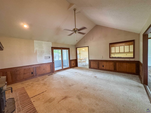 7285 Nowell Rd S, Macon, GA 31216 - unfurnished living room with vaulted ceiling, a wainscoted wall, carpet, a ceiling fan, and a wood stove