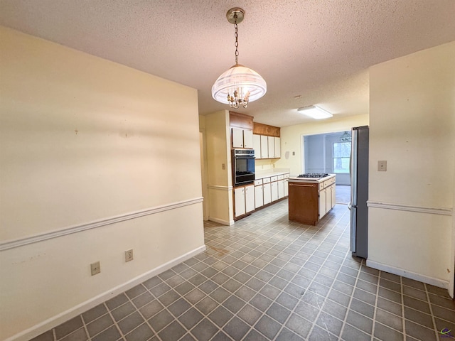 7285 Nowell Rd S, Macon, GA 31216 - kitchen with black oven, freestanding refrigerator, a textured ceiling, a chandelier, and a center island