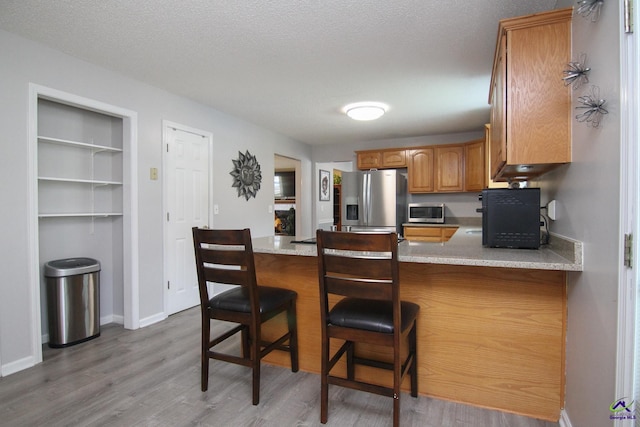 100 Scarlett Dr, Warner Robins, GA 31088 - kitchen featuring stainless steel appliances, a peninsula, brown cabinets, light wood finished floors, and a textured ceiling