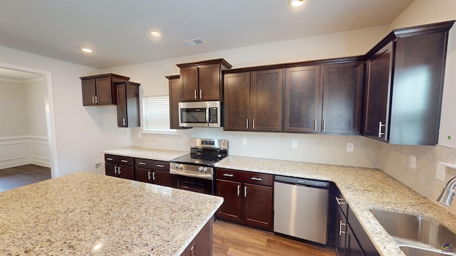 463 Southern Oaks Dr, Macon, GA 31216 - kitchen featuring appliances with stainless steel finishes, wood finished floors, dark brown cabinets, decorative backsplash, and light stone counters