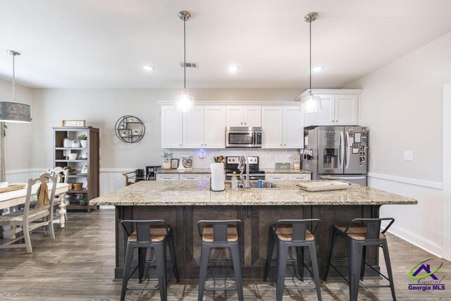 103 Cascades Ct, Bonaire, GA 31005 - kitchen with stainless steel appliances, a center island with sink, dark wood finished floors, white cabinets, and a breakfast bar