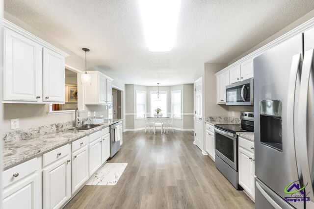 546 Grove Ln, Kathleen, GA 31047 - kitchen with stainless steel appliances, white cabinets, light wood-style floors, hanging light fixtures, and a textured ceiling