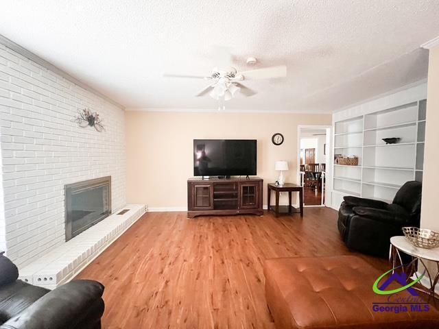 234 Briarcliff Rd, Warner Robins, GA 31088 - living room featuring wood finished floors, a ceiling fan, a brick fireplace, built in features, and a textured ceiling