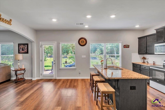 215TYNDALLWAY Tyndall Way, Perry, GA 31069 - kitchen with range with electric cooktop, stainless steel microwave, a breakfast bar area, light stone counters, and light wood-type flooring