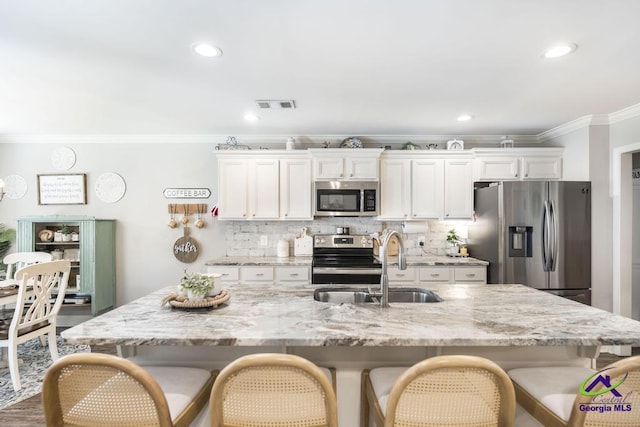306 Gibson Cir, Kathleen, GA 31047 - kitchen featuring stainless steel appliances, crown molding, a breakfast bar area, white cabinetry, and an island with sink