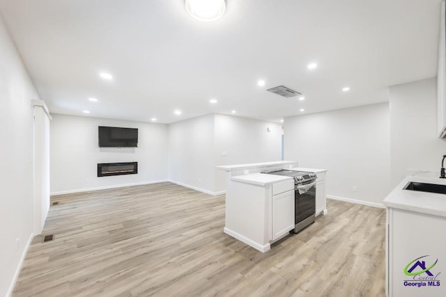 804 Arrowhead Trl, Warner Robins, GA 31088 - kitchen featuring stainless steel electric stove, a glass covered fireplace, light countertops, white cabinetry, and light wood-style flooring