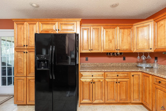 413 Madison Place Parkway, Byron, GA 31008 - kitchen featuring black fridge with ice dispenser, a textured ceiling, light stone countertops, light tile patterned floors, and brown cabinetry