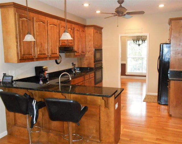 kitchen featuring ceiling fan with notable chandelier, hanging light fixtures, light hardwood / wood-style floors, and black appliances