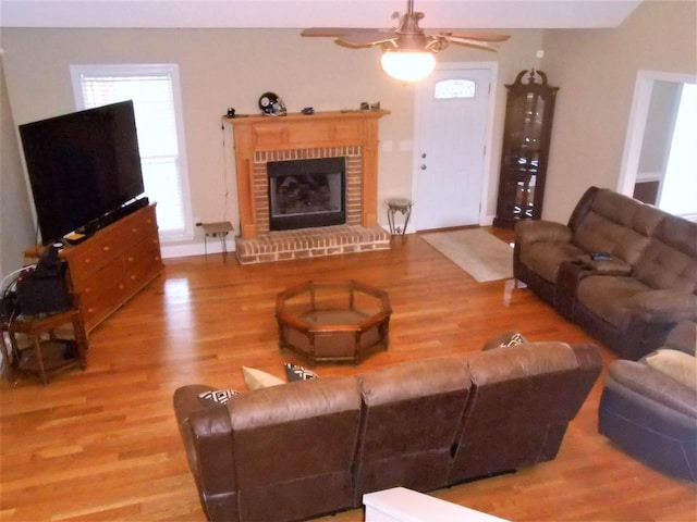 living room with a fireplace, ceiling fan, and light wood-type flooring