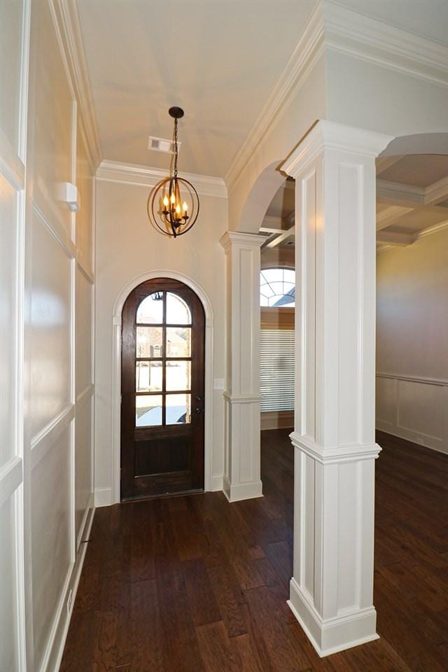 entrance foyer featuring an inviting chandelier, ornate columns, dark hardwood / wood-style flooring, and ornamental molding