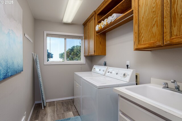 2131 Beach Loop Dr, Bandon, OR 97411 - clothes washing area with baseboards, washer and clothes dryer, light wood-style flooring, cabinet space, and a sink