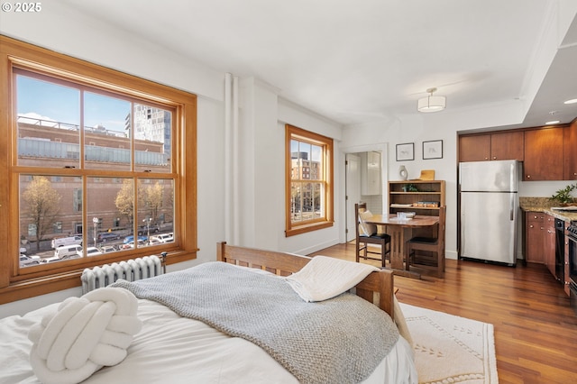 bedroom with baseboards, dark wood-style flooring, radiator heating unit, and freestanding refrigerator