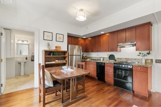 kitchen with wood finished floors, a sink, black appliances, under cabinet range hood, and crown molding