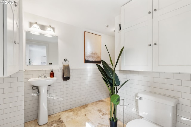 half bath with tile walls, toilet, wainscoting, and a sink