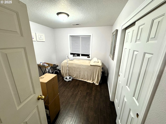 bedroom with dark wood-style floors, a closet, visible vents, and a textured ceiling